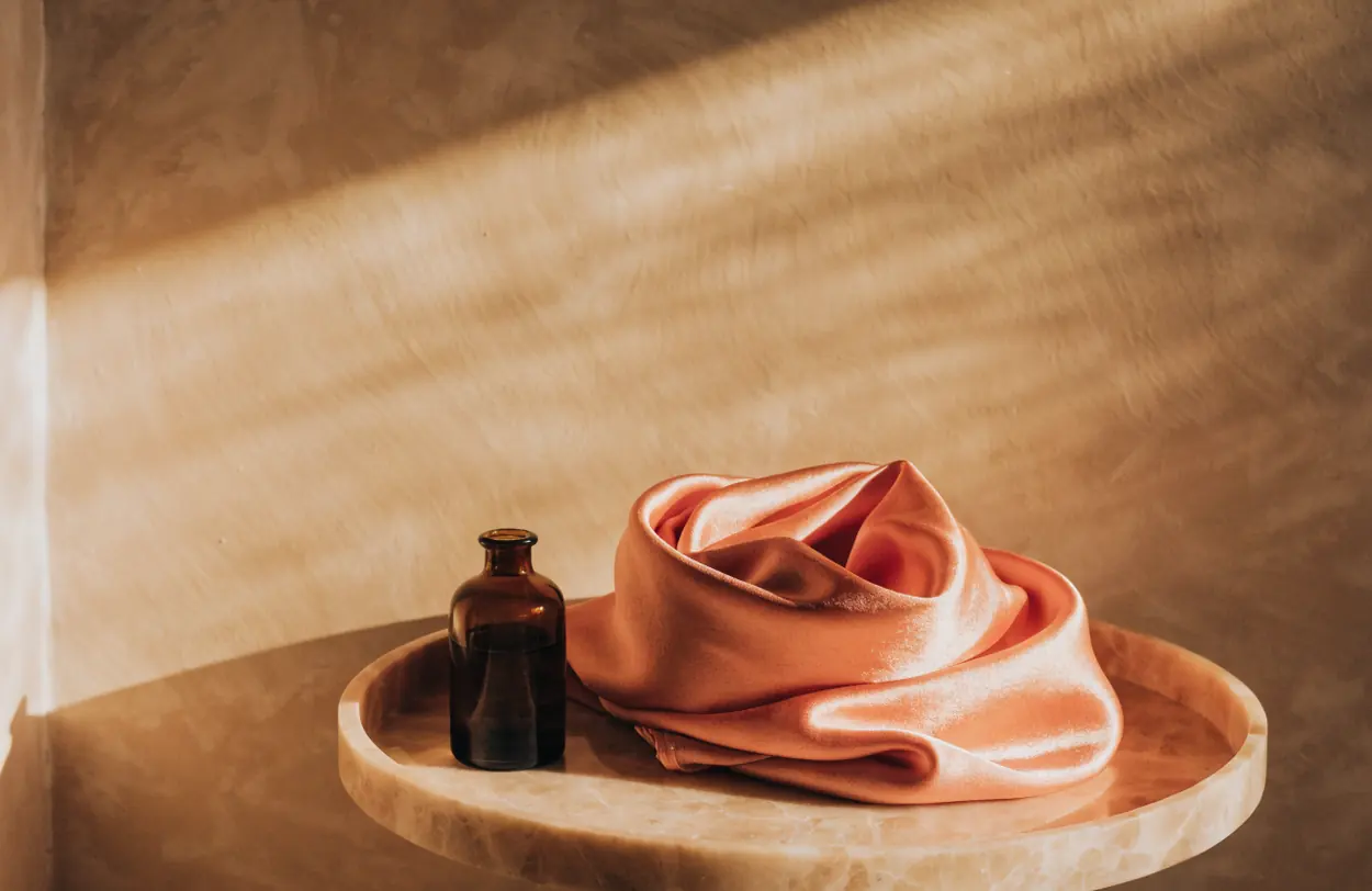 A pale marble tray holding a folded silk scarf and a small frosted glass bottle