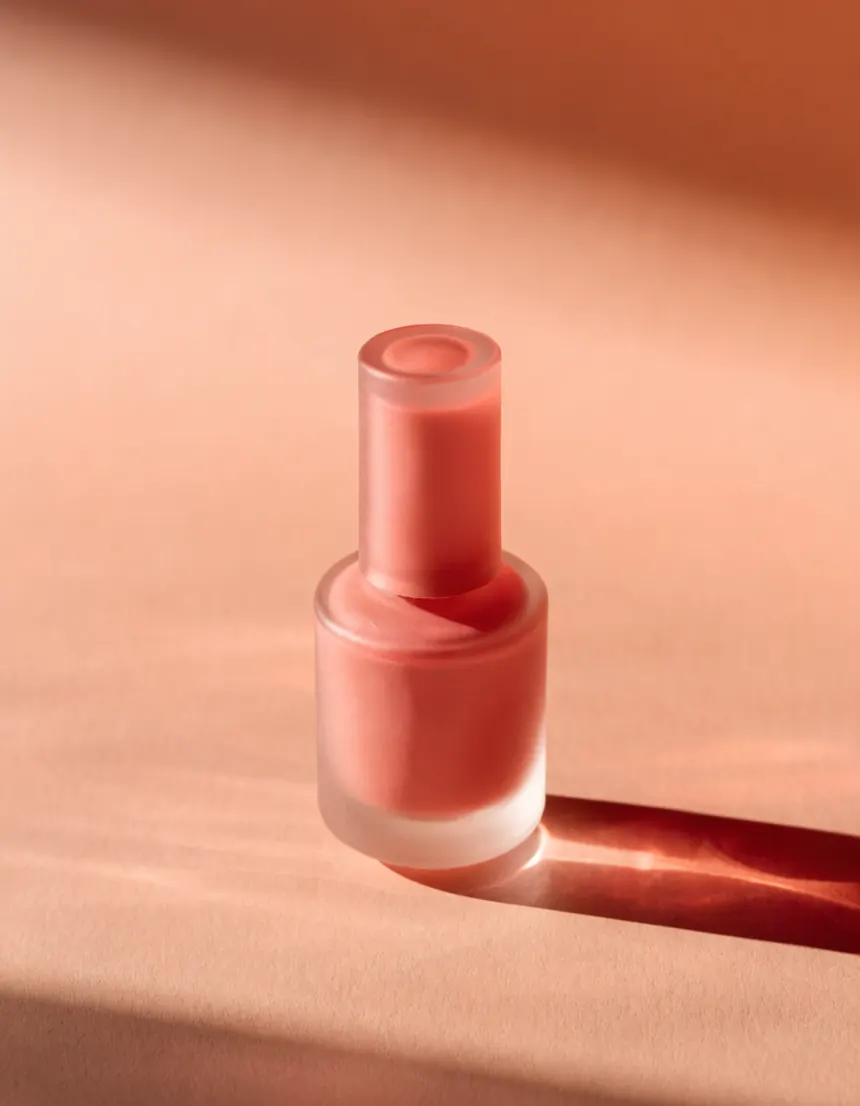 A frosted glass nail polish bottle on pale gray seamless with a long soft shadow
