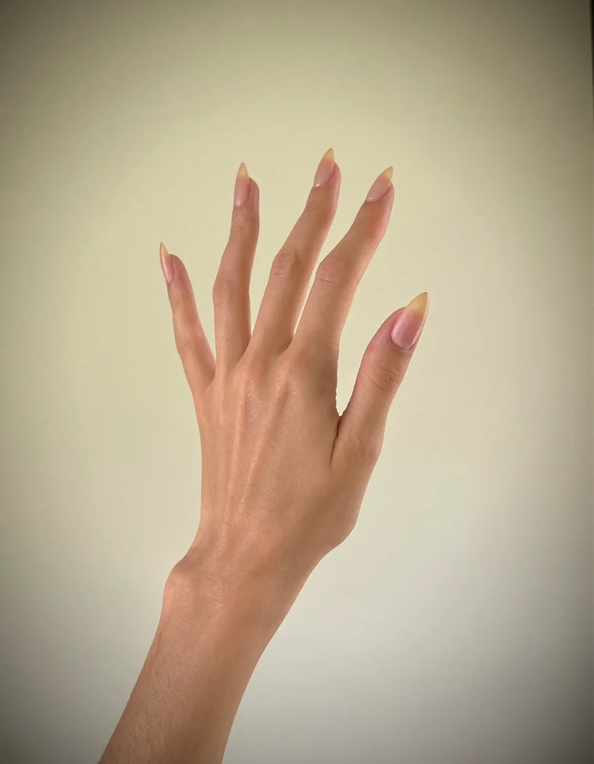 A raised hand with neat natural almond nails against a warm cream backdrop