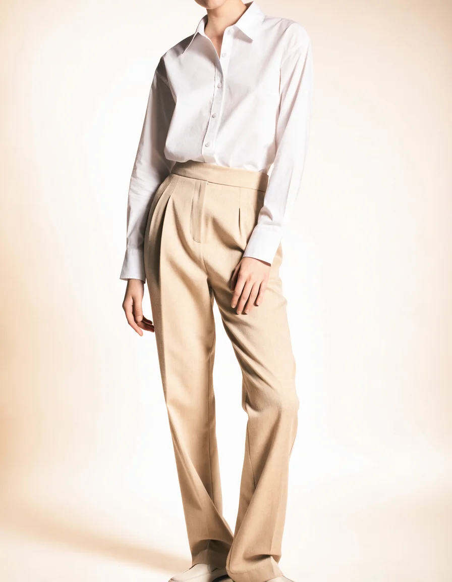 A model wearing a crisp white shirt tucked into softly tailored camel trousers