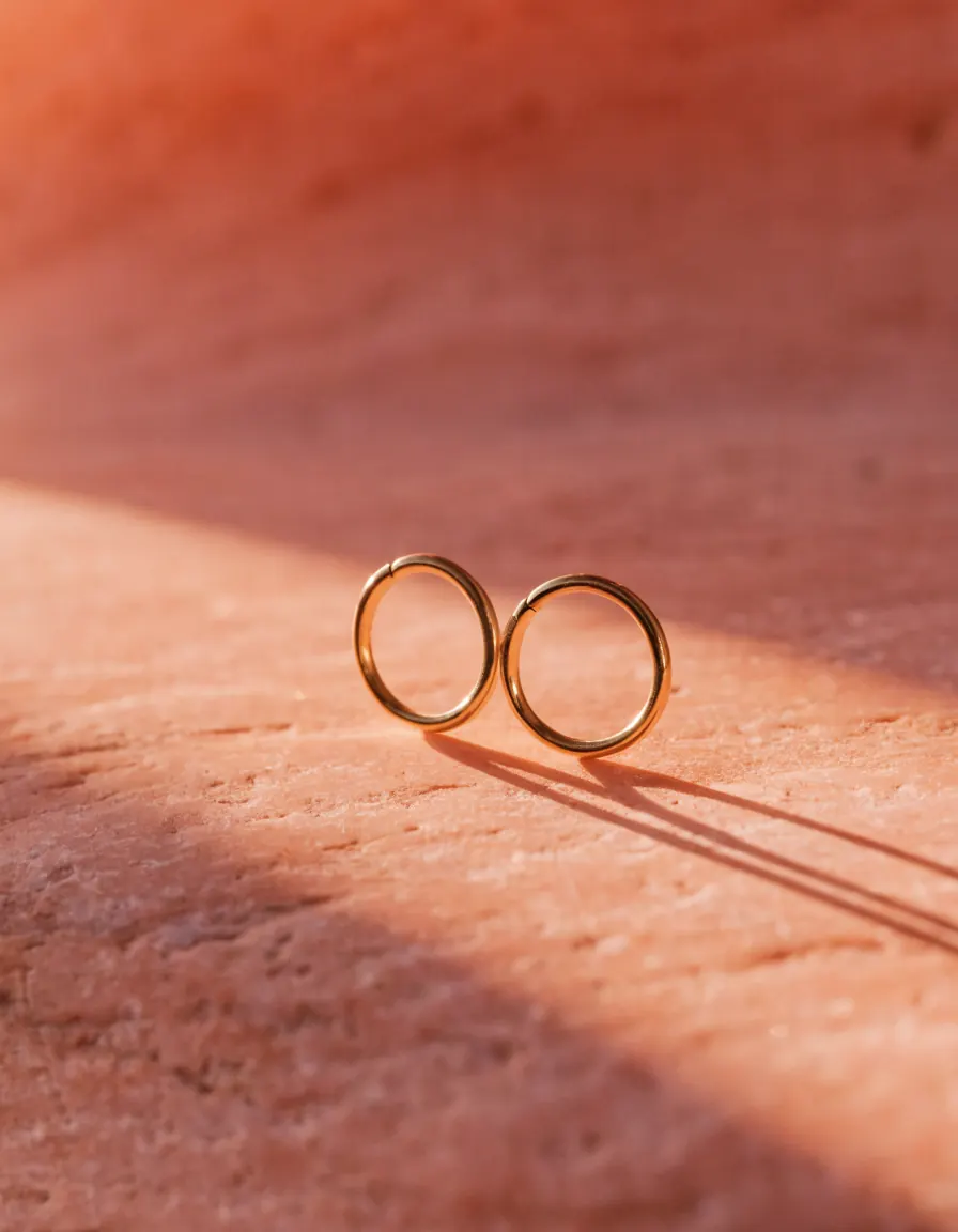 A pair of small gold hoop earrings resting on a pale limestone slab