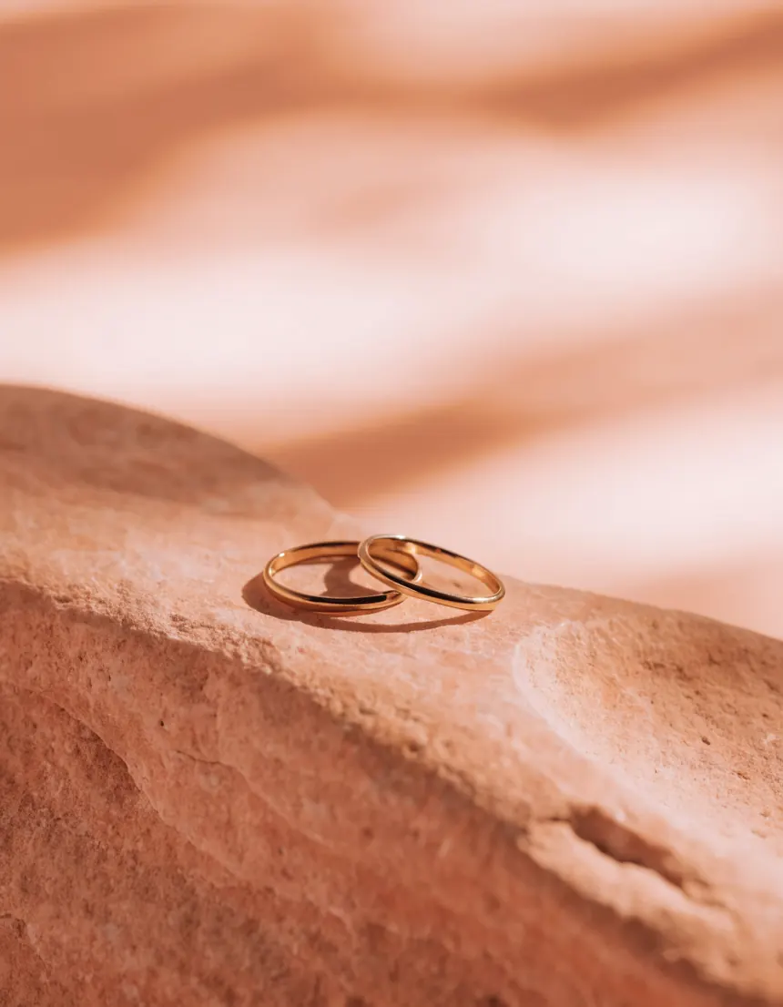 Two gold rings resting on a pale stone slab in soft daylight