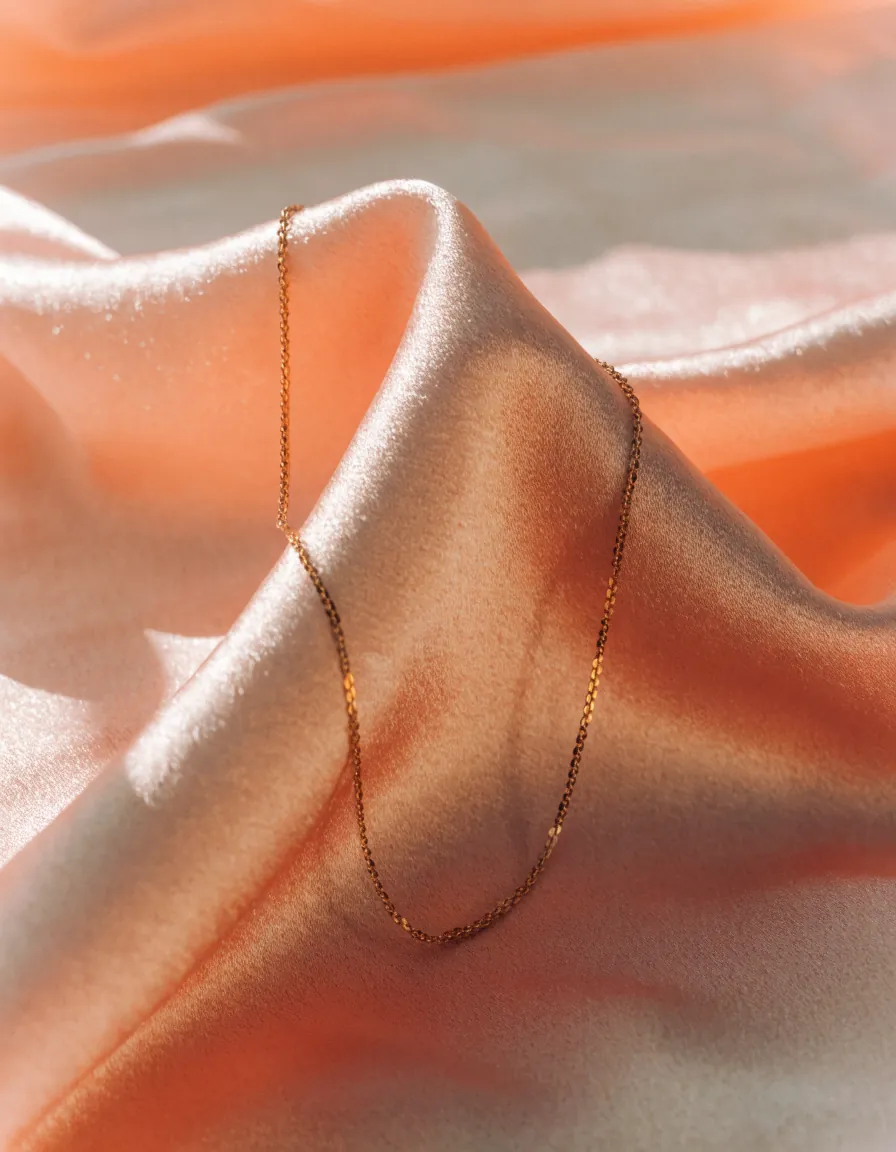 A fine gold chain resting in the folds of ivory silk in soft daylight