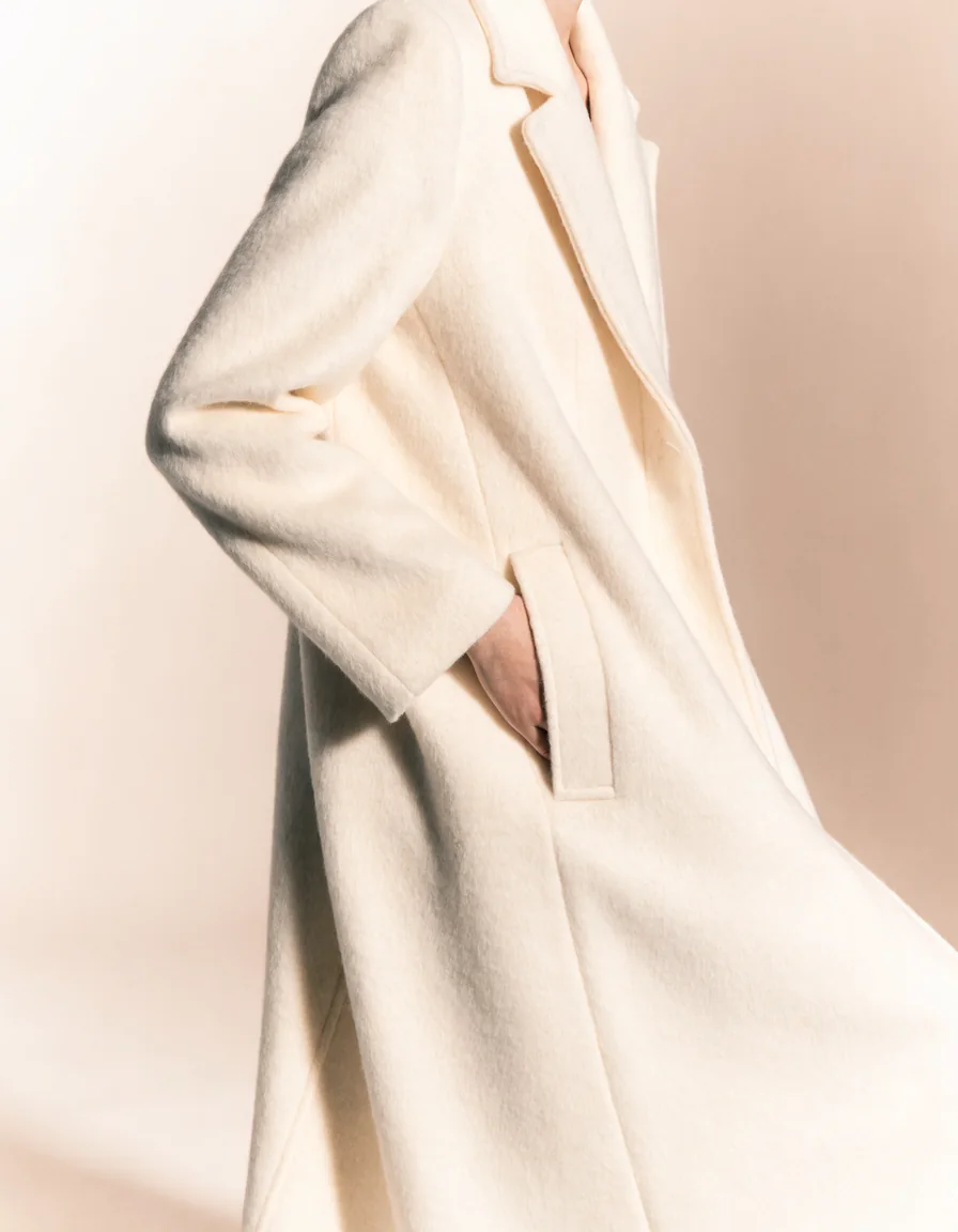 A model wearing an impeccably tailored ivory wool coat, one hand in the pocket