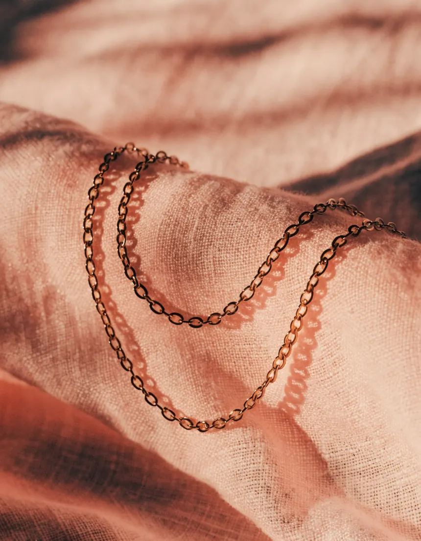 Two fine gold chain necklaces layered together on pale gray linen